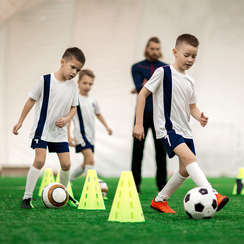 Active boys in uniform training with balls while running by soccer cones on green field